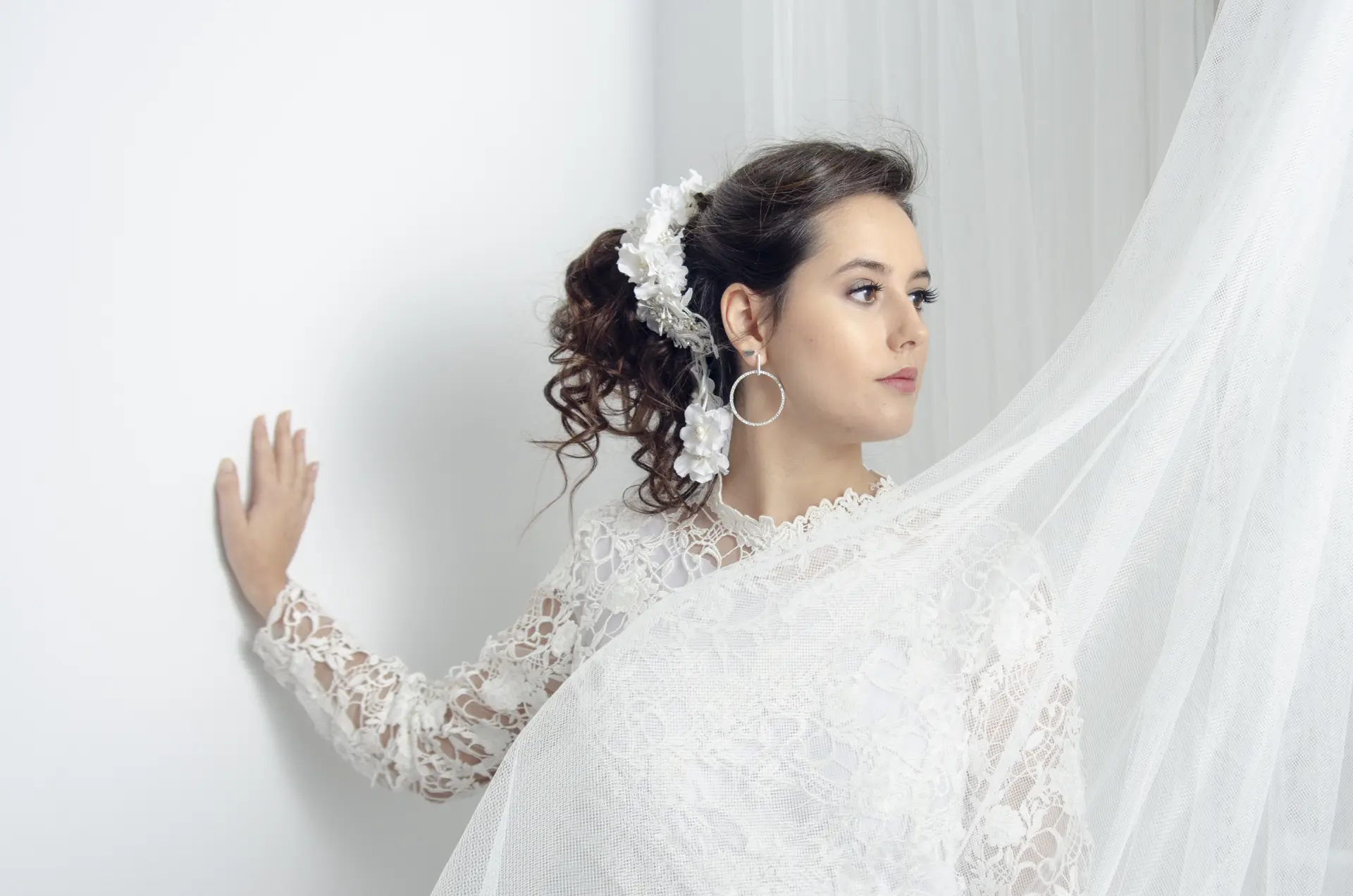 Editorial bridal photograph of model in white lace gown with veil against soft white drapery