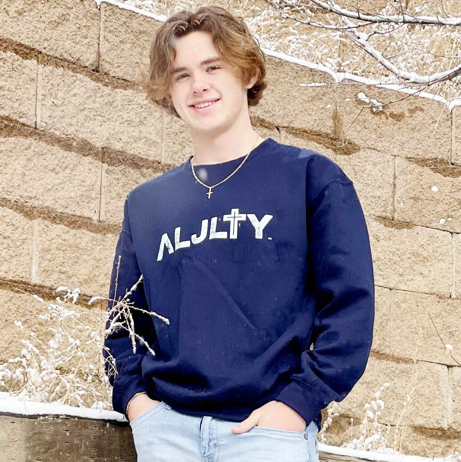 Brenton in a navy ALJLTY sweater against a stone wall with snow