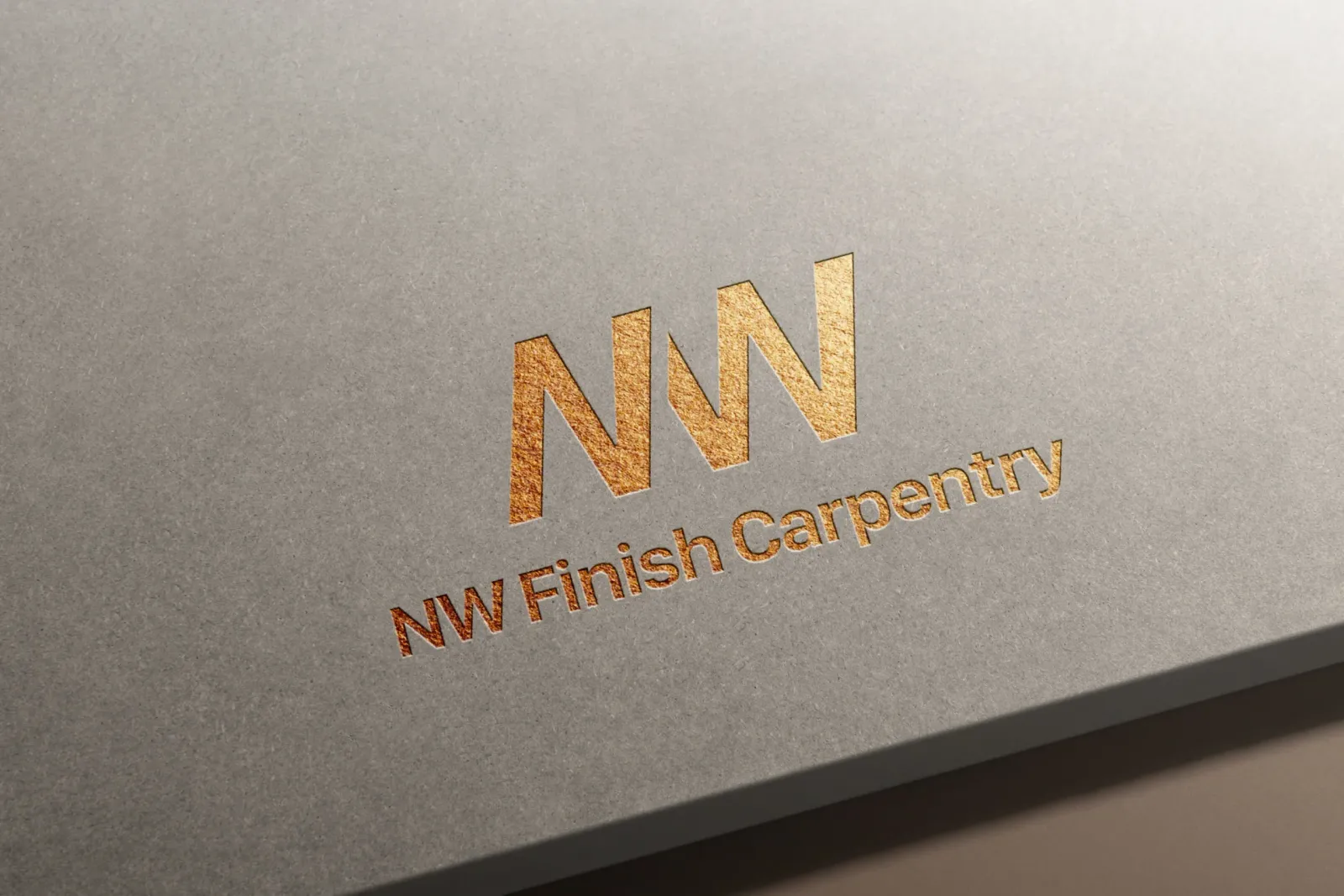 Gold foil embossed NW Finish Carpentry logo on smooth gray cardstock, showing the stylized NW monogram with saw blade-inspired angular letterforms above the company name in elegant metallic serif typography