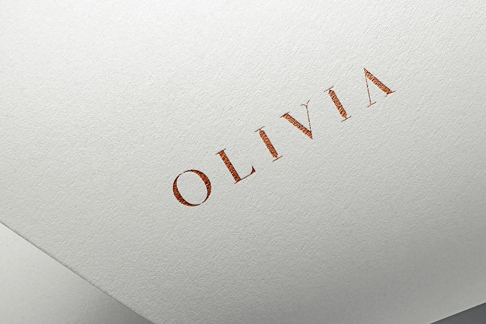 Olivia custom serif wordmark in copper foil on textured white paper showing letter detail